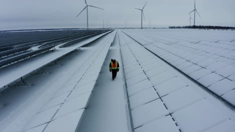 worker inspecting snow-covered solar panels and wind turbines in winter