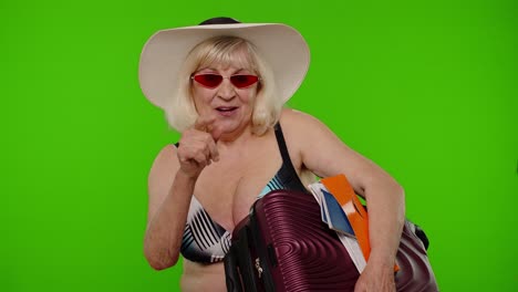 Senior-woman-tourist-in-swimsuit-with-luggage,-passport,-tickets-asking-to-follow-join-on-chroma-key