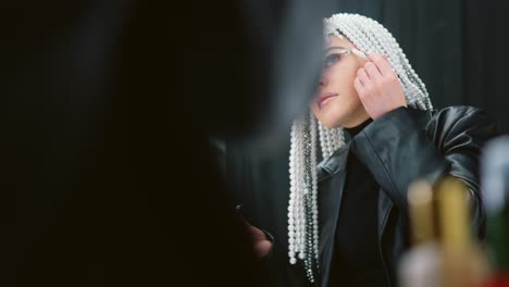 woman with pearl adorned dreadlocks applying glitter makeup