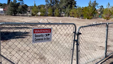 cámaras de seguridad de advertencia en uso de señalización en una cerca de eslabones de cadena en el desierto alto frente a un lote vacío a mediodía