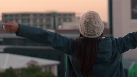 rear view happy woman arms raised celebrating freedom on rooftop enjoying independent lifestyle achievement in urban city