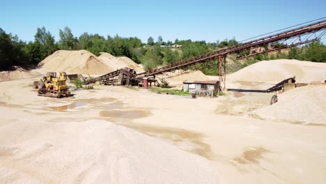 sand mounds, a bulldozer, and a conveyor belt in an old sand mine near the town of prudnik, poland - drone flying forward