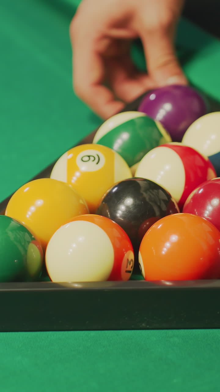 Close-up of hand rolling a well-arranged set of colorful billiard balls in triangle formation on green pool table. The vibrant balls are precisely aligned, capturing a moment of focus and preparation