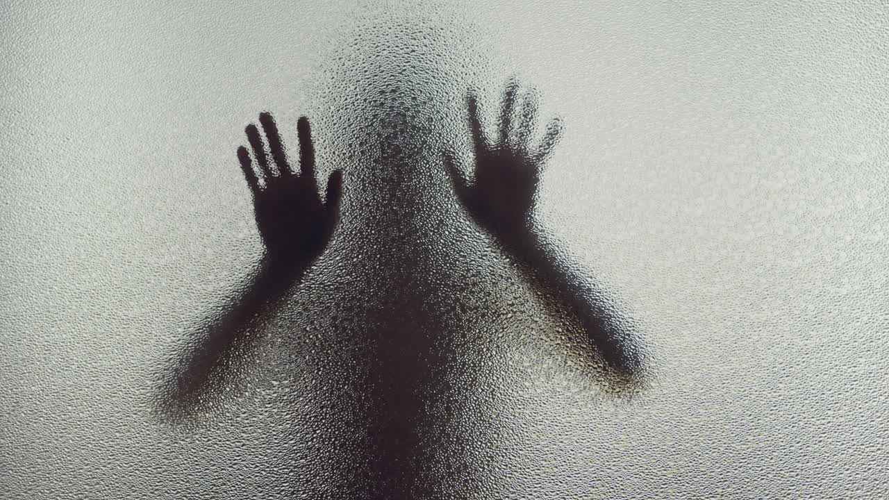 A female silhouette behind the frosted glass moves slowly and kiss the glass