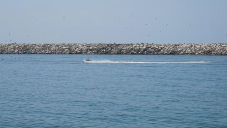 jetski conduciendo rápido hacia el puerto superando un viejo barco
