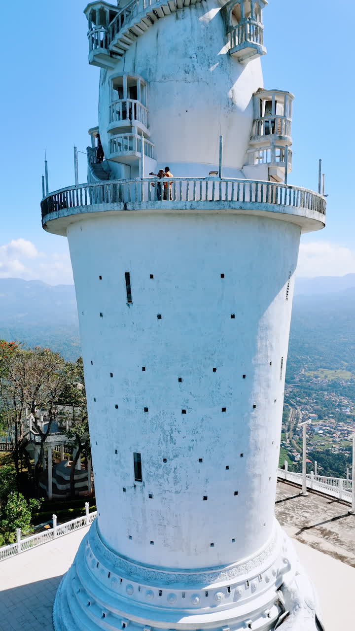 Rising along the white Tower of Ambuluwawa Temple. Tourist go up by the winding stairs of the building. Sun dazzled scenery of Gampola Town, Sri Lanka at backdrop. Vertical video.