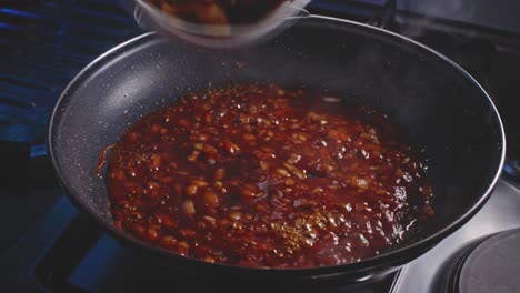 Adding-fried-chicken-pieces-to-frying-pan-with-tomato-sauce-and-onion-pieces-on-it,-close-up-view