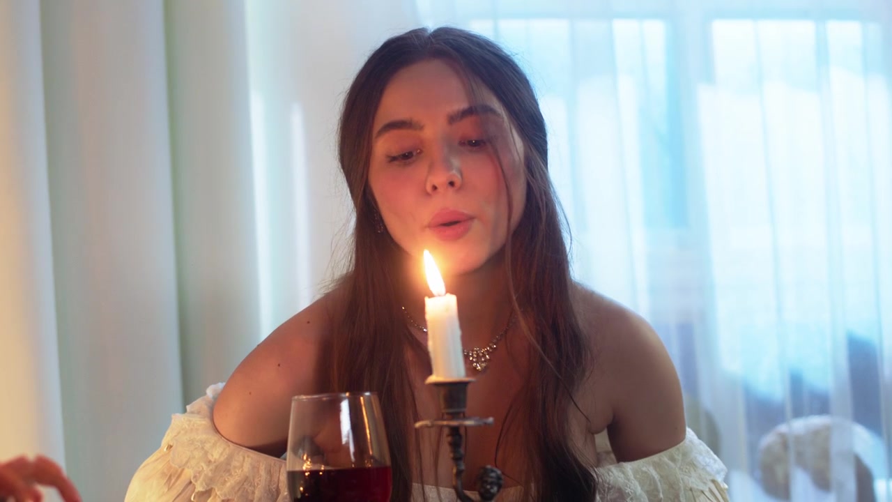 Giovane donna spegne una candela e sorride alla telecamera.