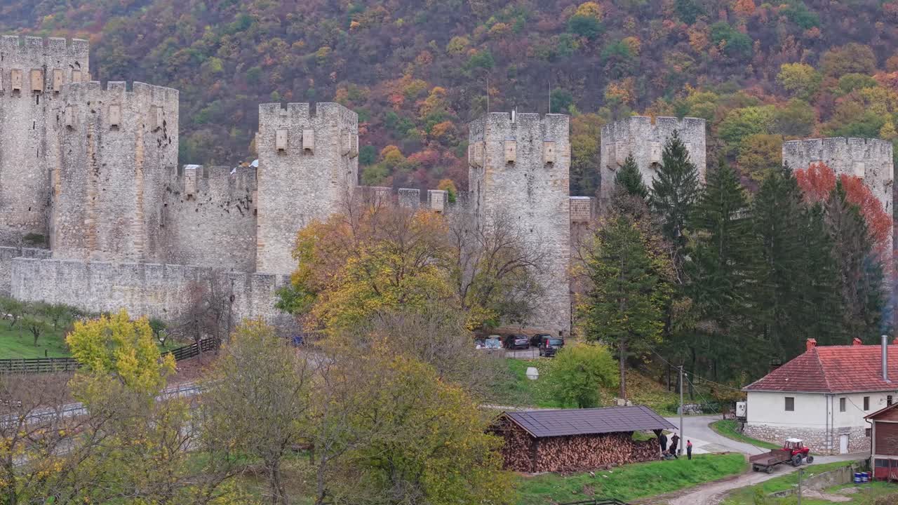 Boční sledovací záběr odhalující mohutné středověké obranné zdi a opevněné věže kláštera Manasija. Dron se pohybuje do strany a ukazuje rozsah kamenných hradeb z 15. století