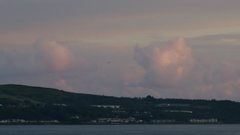 Timelapse-Nubes-Rosadas-Pasando-Sobre-Agua-Y-Tierra-Y-Ciudad-Distante-En-Verano