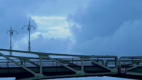 Hermosas-Nubes-De-Lluvia-Gris-Oscuro-Que-Se-Mueven-Rápidamente-Sobre-El-Puente-Oscilante-Oskara-Kalpaka-En-La-Ciudad-De-Liepaja-Por-La-Noche,-Plano-Medio