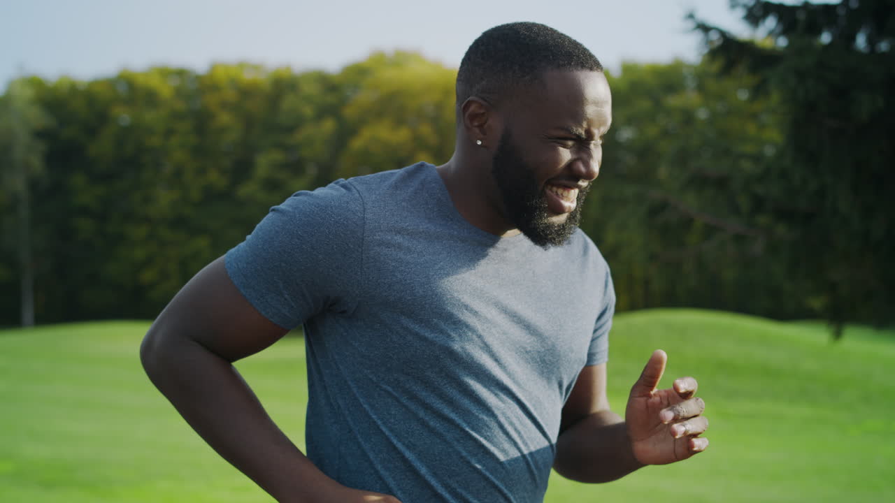 Tired male athlete running in park. Afro guy training in green area