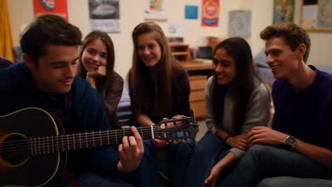 young people playing guitar and singing together in a dorm room
