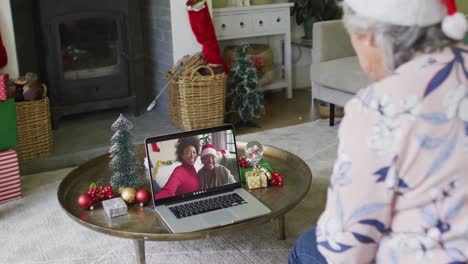 Caucasian-senior-woman-with-santa-hat-using-laptop-for-christmas-video-call-with-family-on-screen