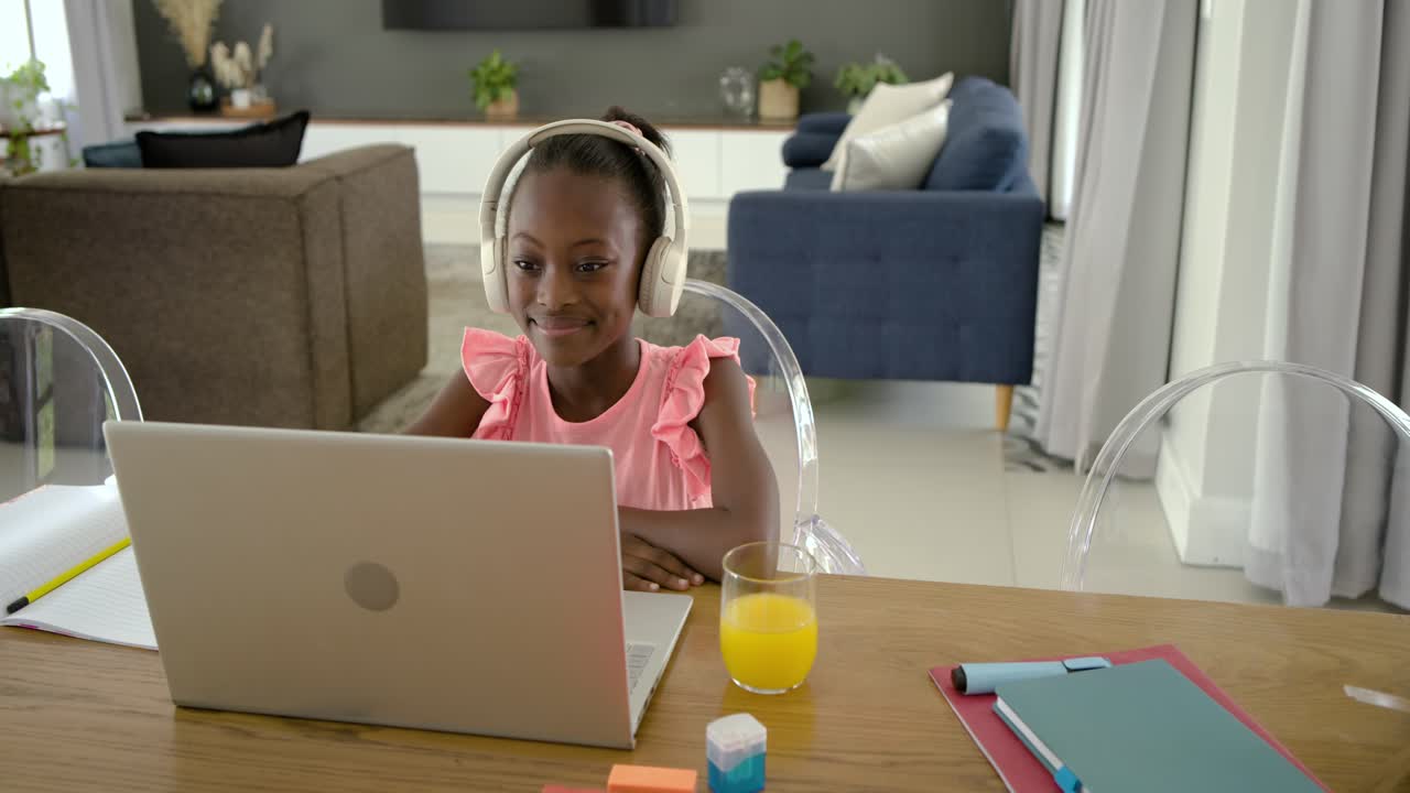 African female youth seeing headphones reaching placing on head joining laptop call at dining table