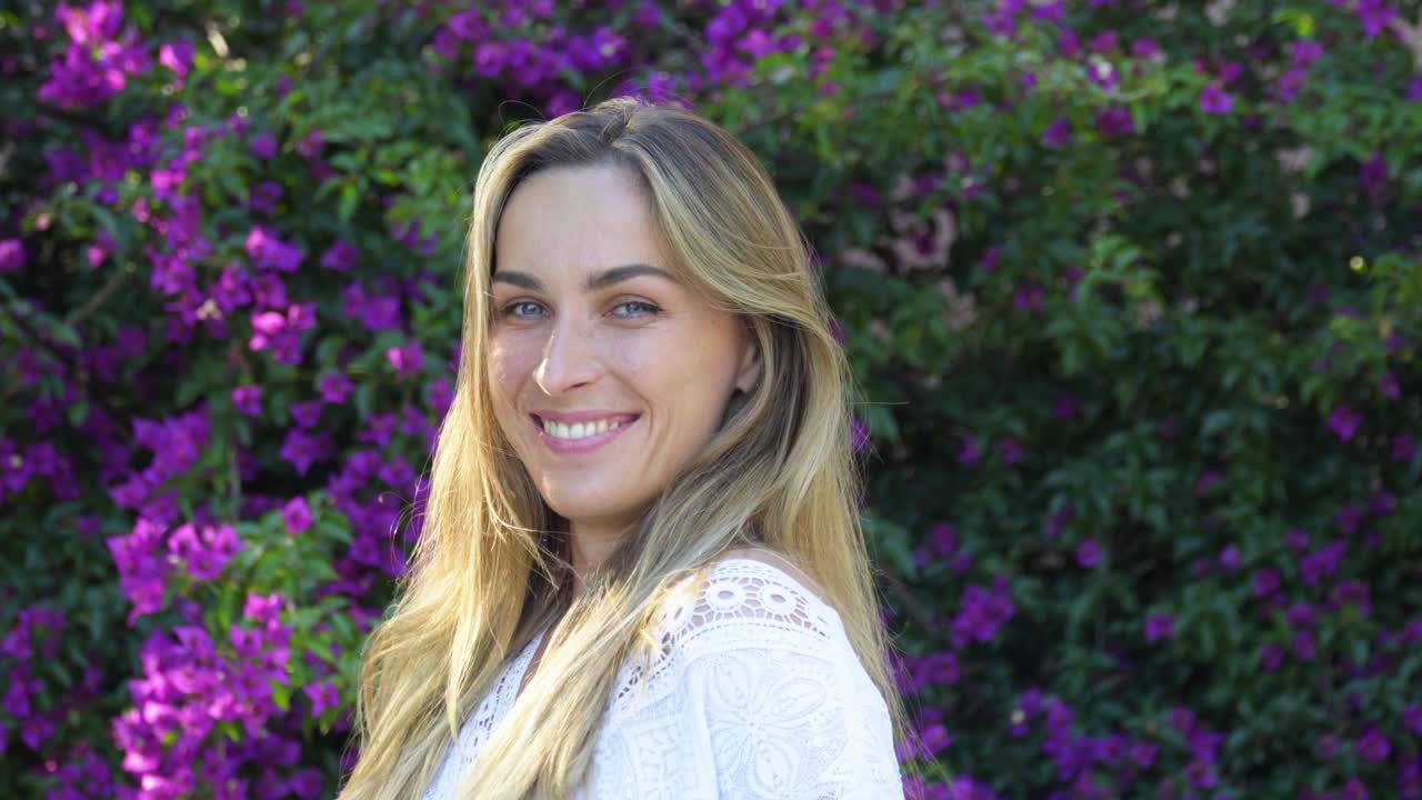 Retrato de una mujer rubia de ojos azules y alegre con una hermosa sonrisa posando con un vestido blanco, mirando a la cámara y sonriendo