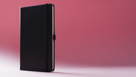 closed black notebook standing vertical with copy space on red background in slow motion