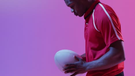 african american male rugby player with rugby ball over pink lighting