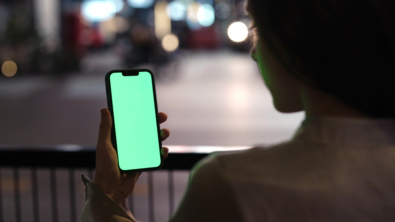 Mujer usando un smartphone con pantalla verde con luces de la ciudad por la noche