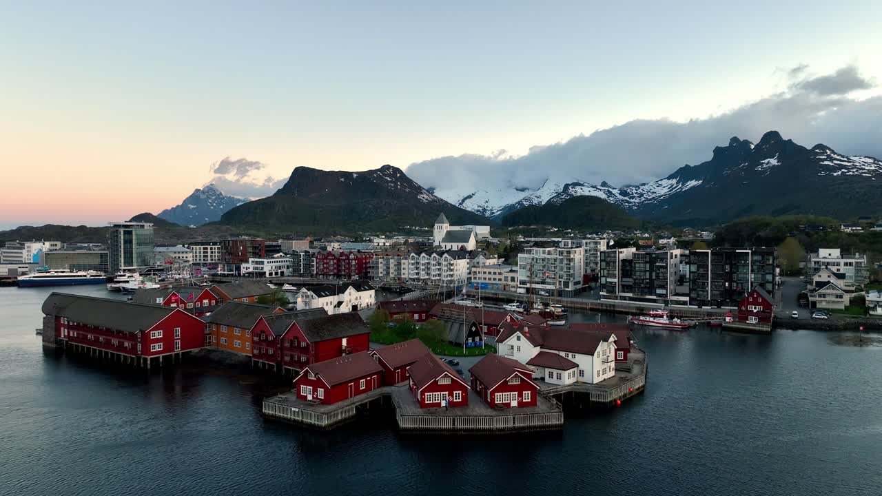 Drone flies toward Lamholmen in Svolvaer with Storoya church and city in soft midnight sun light
