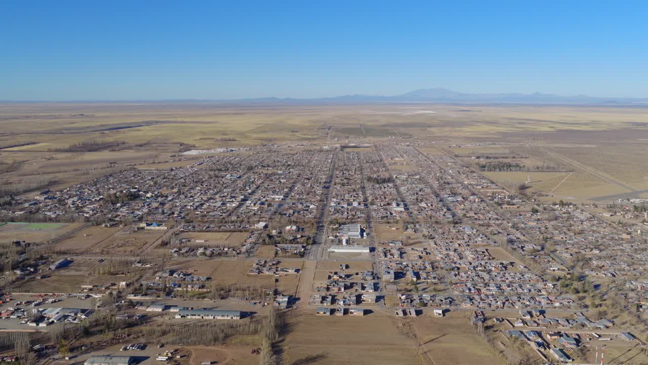 Drone pans slowly across Malargüe in Mendoza, Argentina, revealing the structured city grid surrounded by dry farmland and open plains under clear skies in the arid Andean foothills region.
