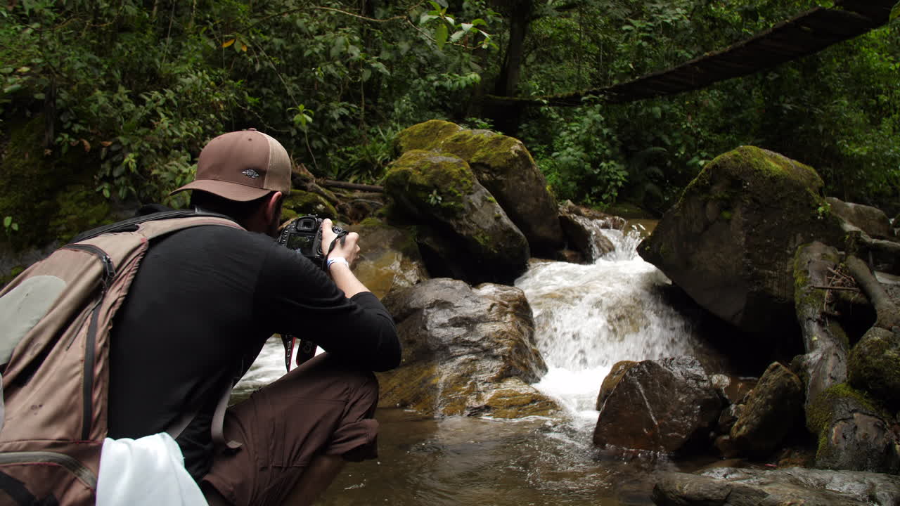 fotógrafo tomando fotos de un río que corre bajo un puente en la jungla