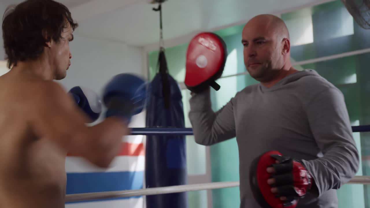 Uomo caucasico che si allena con l'allenatore sul ring di pugilato