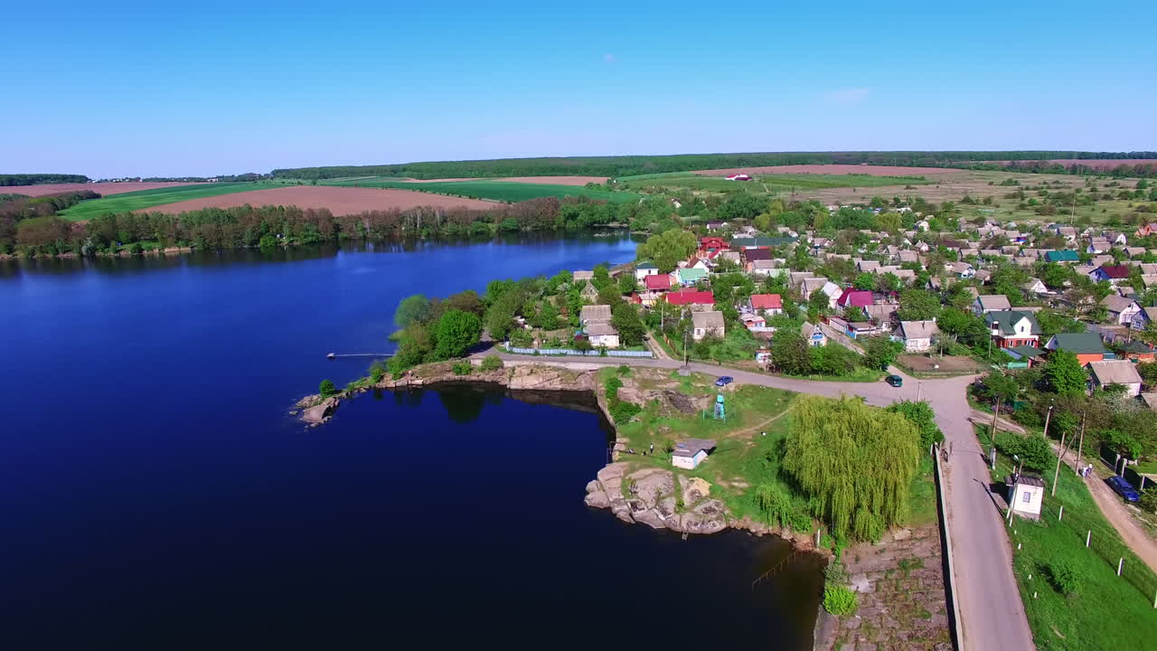 Contrasting azure surface of the river near the green bank. Cute cozy village with beautiful houses on bright sunny daytime from top.