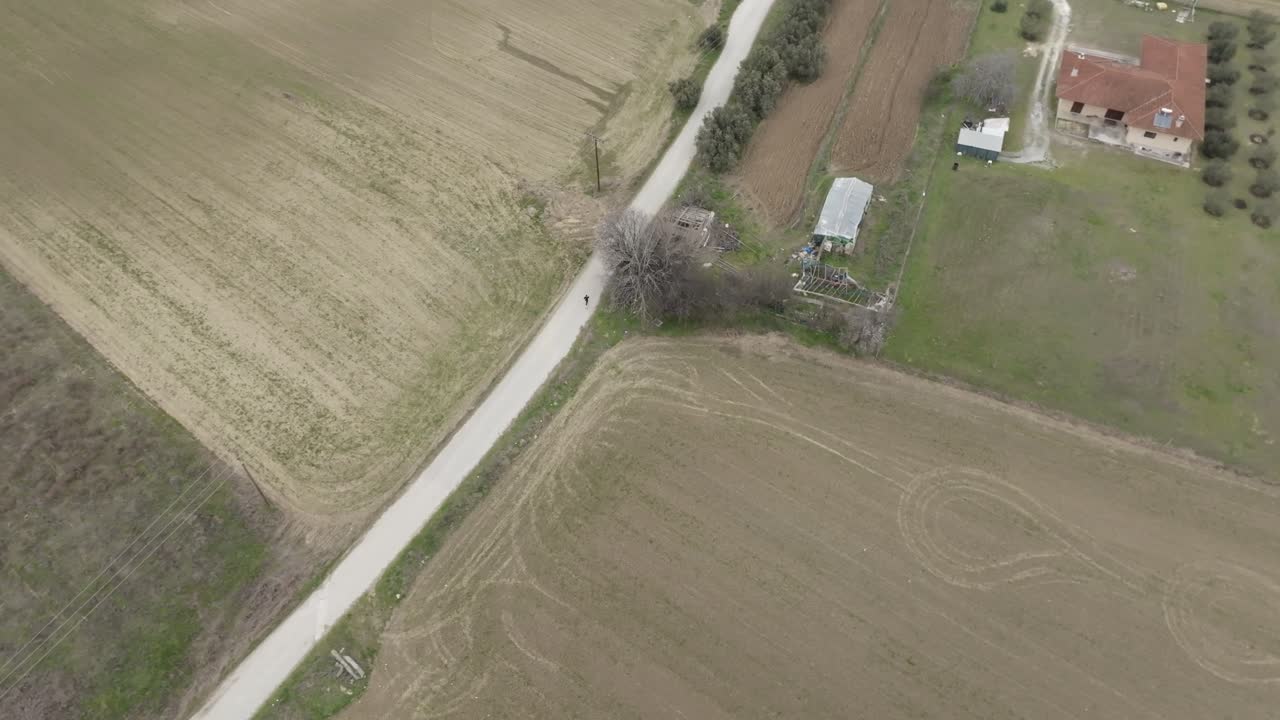Top-down aerial drone view of person running on rural road, surrounded by open fields and farm landscapes.