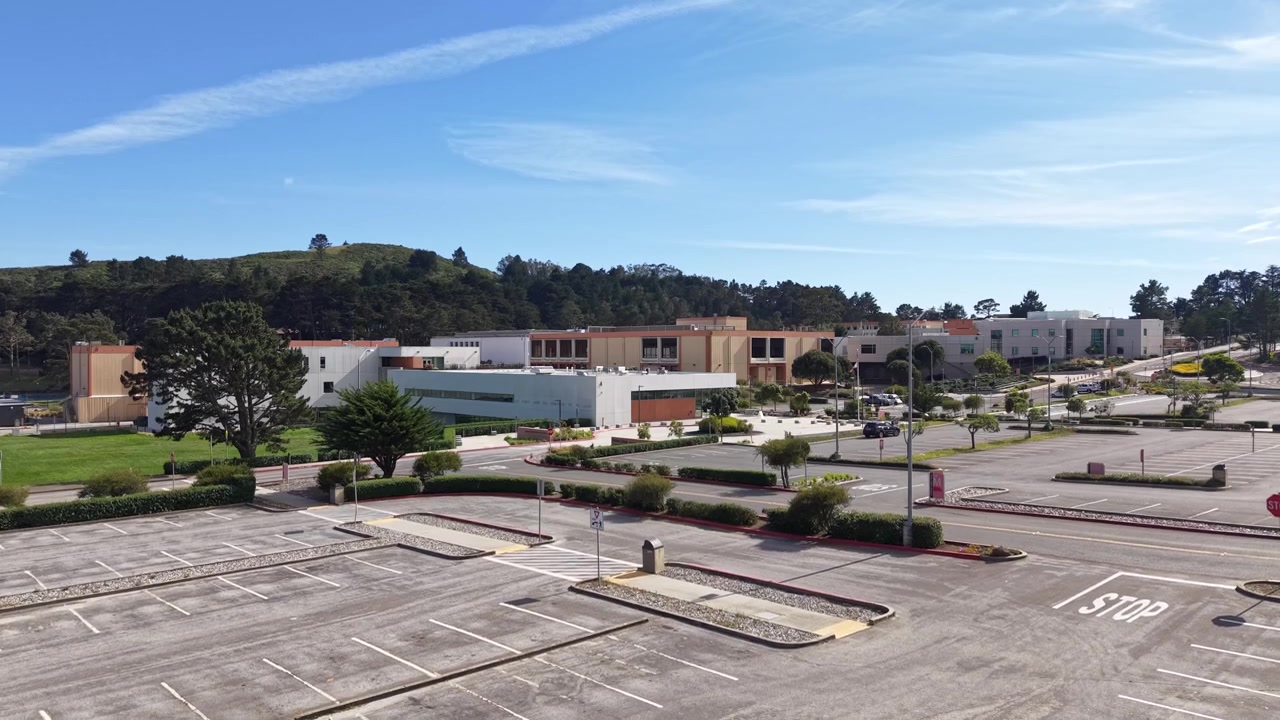 Vista aérea del campus casi desierto de Skyline College y el estacionamiento vacío en un día soleado en San Bruno, California, mostrando la quietud de las instalaciones académicas durante un receso