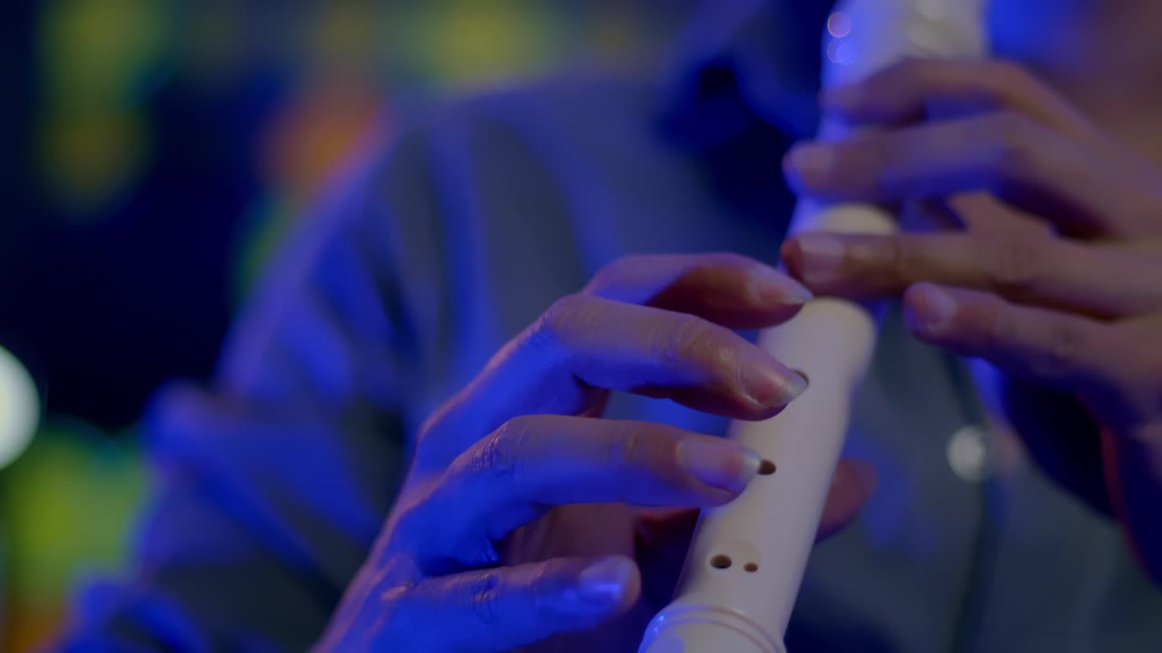 Plan au ralenti d'un musicien jouant de la flûte à bec, lumières colorées floues en arrière-plan.