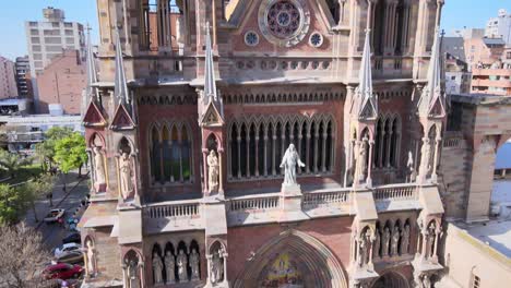 Aerial-elevation-shot-overlooking-the-main-facade-of-roman-catholic-Sacred-Heart-Church-of-the-Capuchin-Fathers,-neo-gothic-architecture-style,-reveals-crowded-downtown-cityscape-of-Cordoba-city