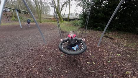 slow motion video of a young boy having fun in a playground swinging and laughing surrounded by autumn leaves