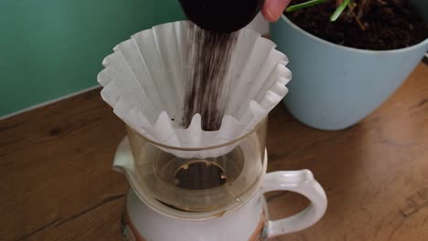 close up: ground coffee poured into basket filter on small coffee pot