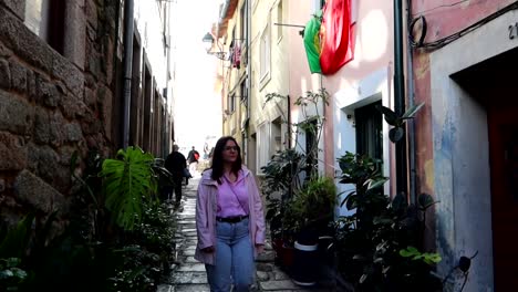 woman walking down a narrow cobbled alley of rua das aldas, portuguese flag waving on a facade