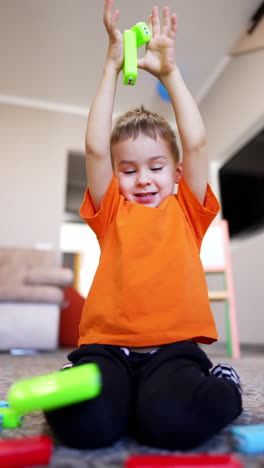 caucasian baby boy wearing orange t-shirt and black pants sits on the floor. happy toddler plays with colorful bricks. low angle view. vertical video.