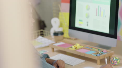 joven mujer de negocios afroamericana usando computadora haciendo lluvia de ideas navegando en línea ideas de investigación para una empresa nueva escuchando música usando auriculares en una oficina moderna y colorida