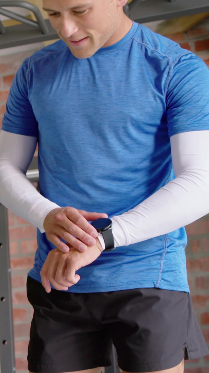 Video verticale: Uomo con camicia blu e maniche bianche che guarda lo smartwatch e controlla le metriche in palestra.