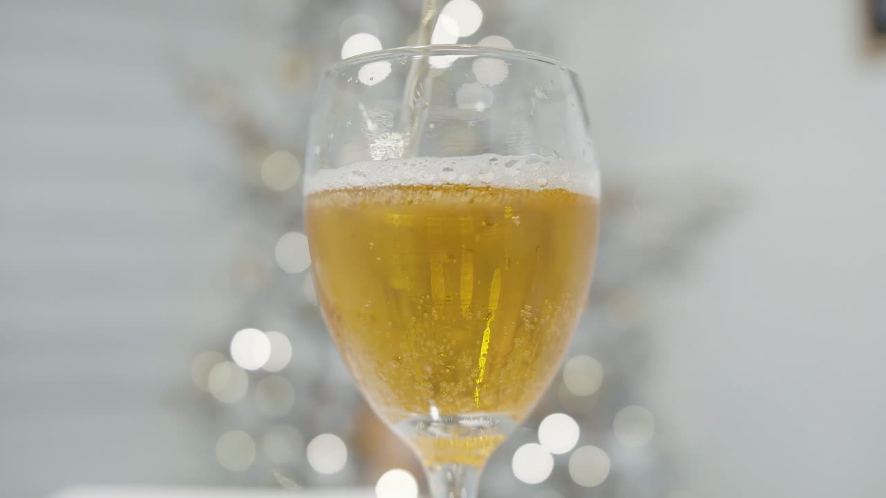 Hand gießt Bier in ein Glas mit unscharfem Weihnachtsbaum im Hintergrund, in Zeitlupe