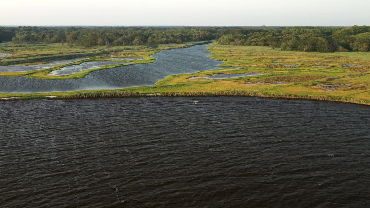 Ripresa aerea discendente sopra le acque del Parco Marina di East Islip, con focus sull'area della palude e un canale navigabile più ampio sulla sinistra, al tramonto.