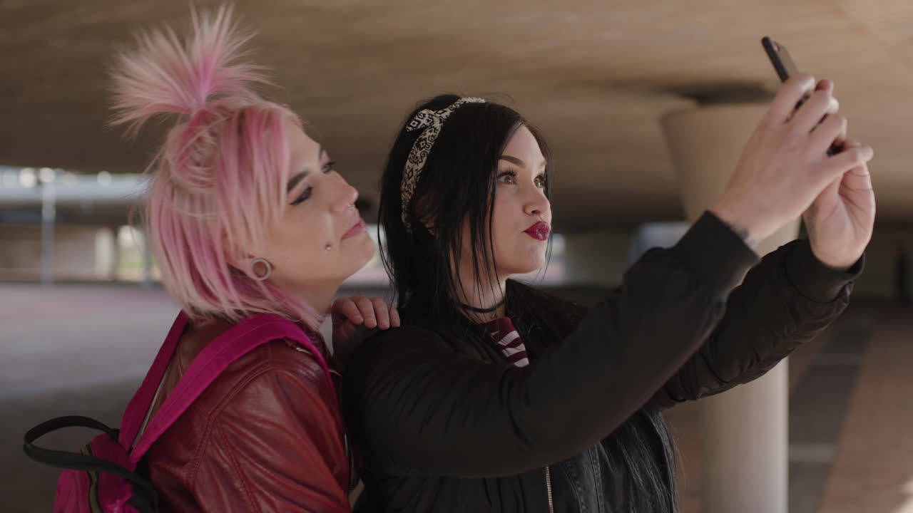 retrato alegre de dos amigas auténticas que usan moda grunge alternativa sonriendo usando el teléfono posando para una foto selfie