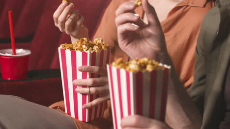 close up view of couple hands holding popcorn in the cinema