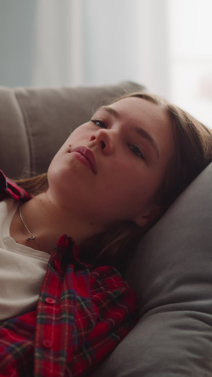 Thoughtful young woman in casual clothes dreams on comfortable sofa in apartment closeup slow motion. Tired lady spends time at cozy place to rest