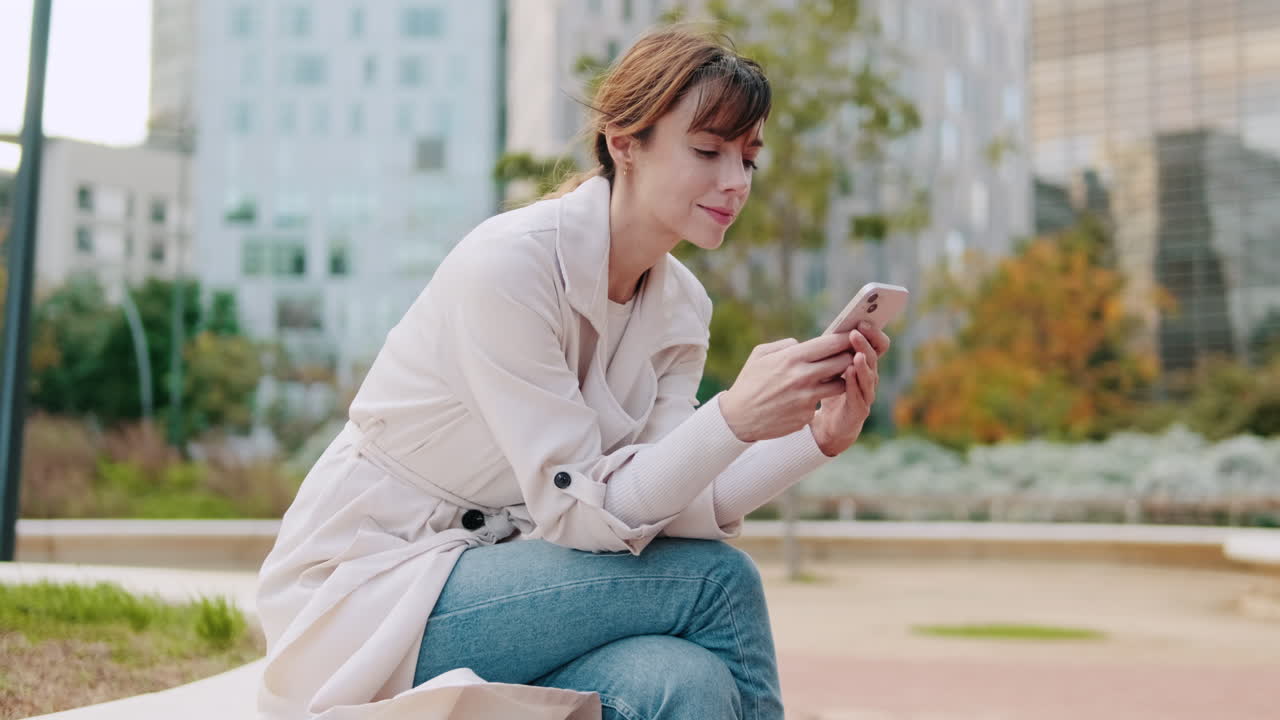 Young Woman Sitting on a Bench and Using Her Smartphone in an Urban Park