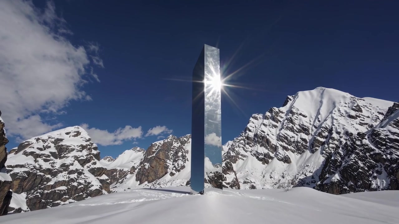 बर्फीले पहाड़ी परिदृश्य में खड़ा परावर्तक मोनोलिथ
