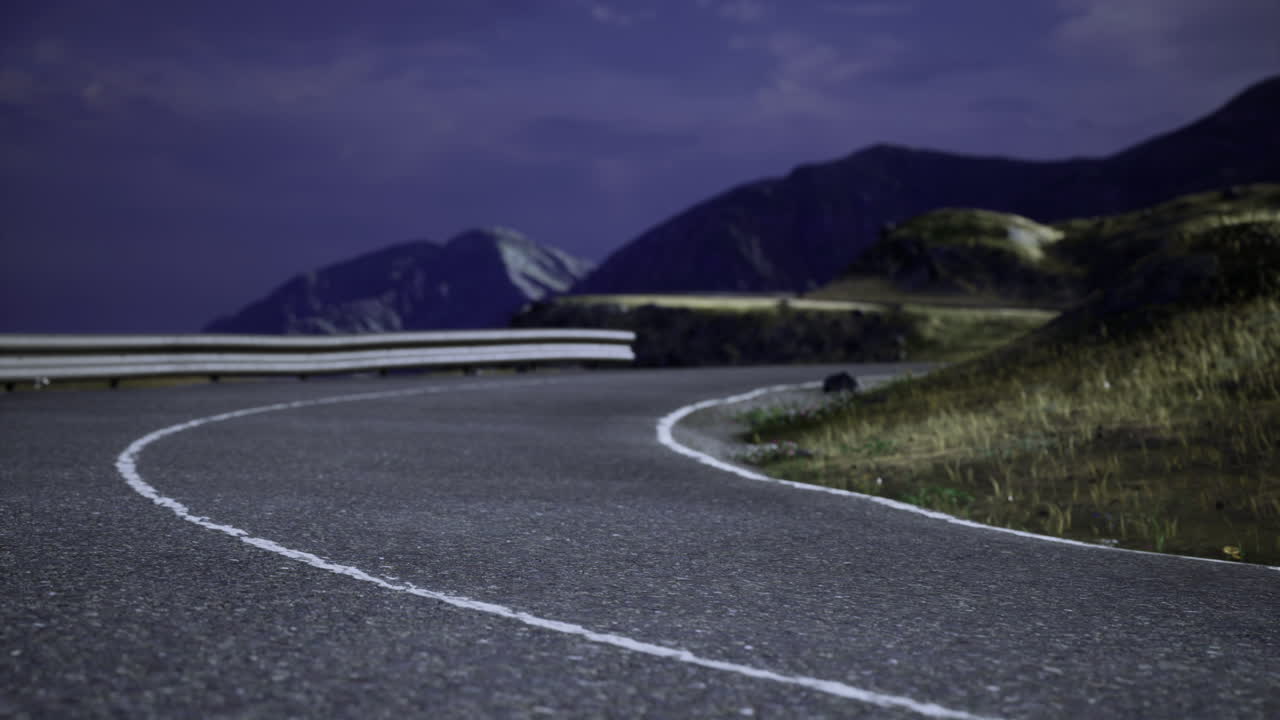 Winding mountain road at night under a starry sky with distant peaks