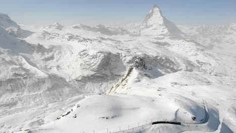 sobrevuelo aéreo sobre gornergrat durante el invierno con vistas al matterhorn y un tren descendente