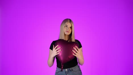 Modelo-Femenino-Caucásico-Joven-Rubio-Sostiene-Un-Globo-En-Forma-De-Corazón-En-El-Fondo-Violeta-Infinito-Del-Estudio-Del-Amor,-Tiro-Del-Torso