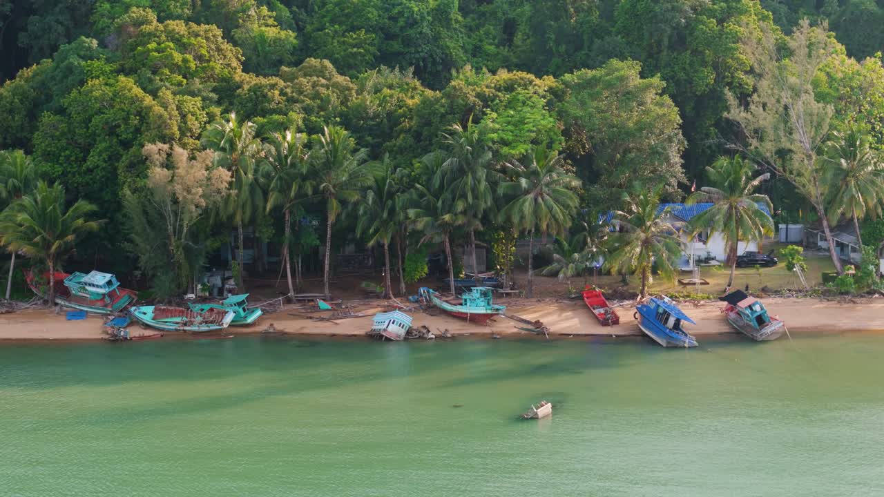 Slow lateral drone flight over tropical beach with abandoned fishing vessels and sunken boat in shallow turquoise waters