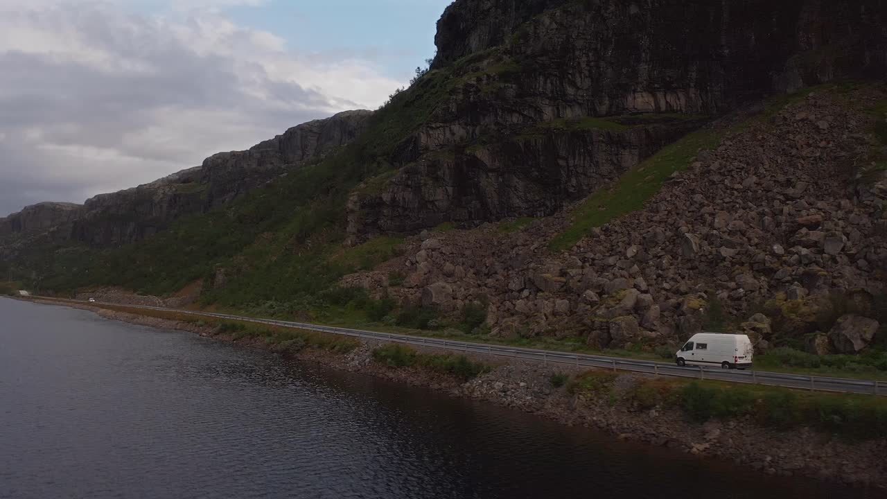 Scenic shot of a van driving along a coastal road in Norway, surrounded by mountains